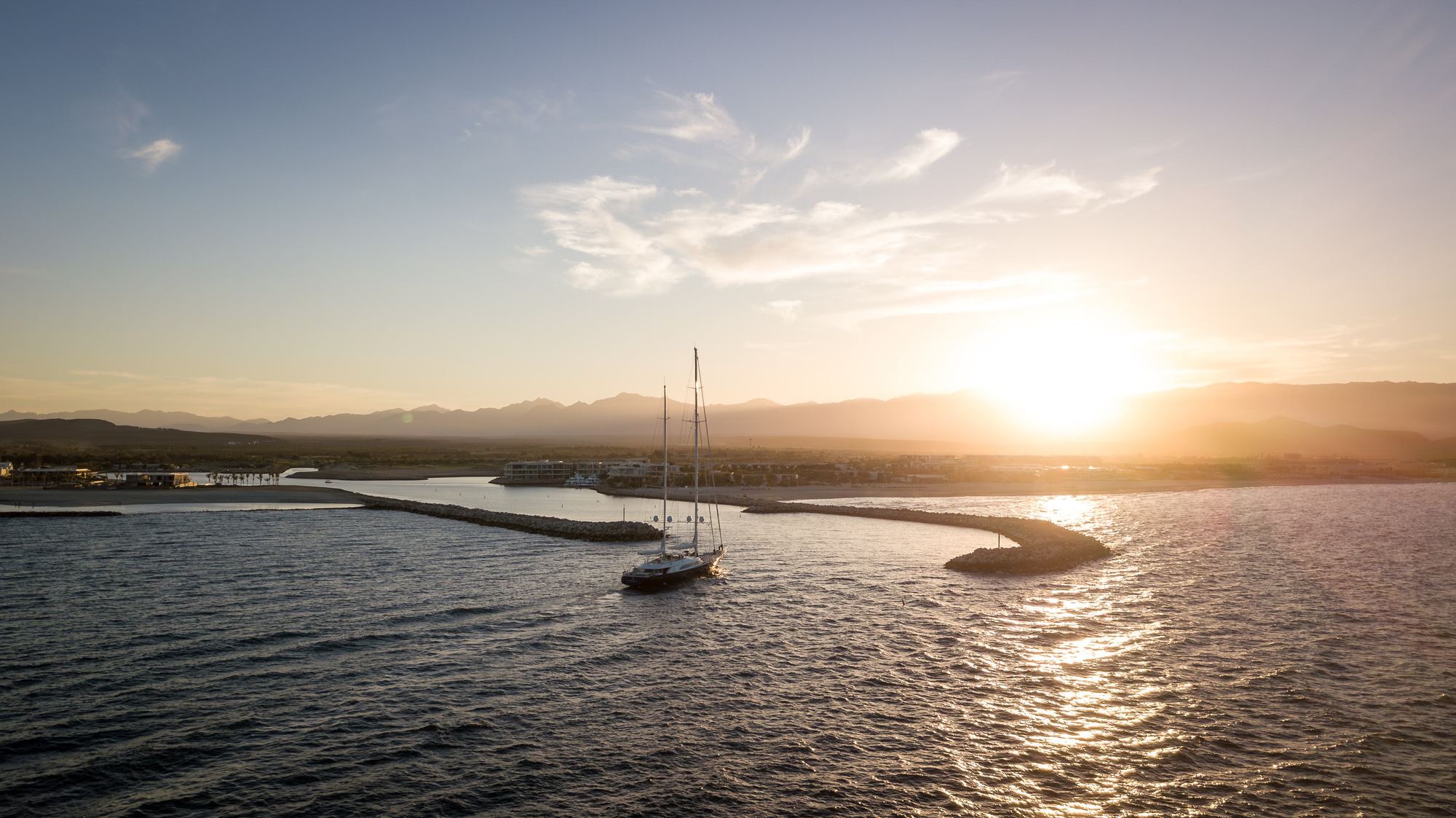 A sailboat entering the Costa Palmas marina at sunset