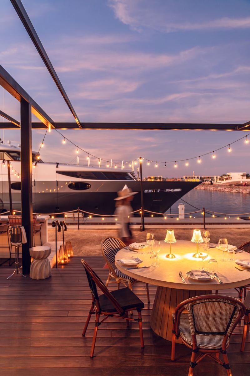 A candlelit table at dusk beside a yacht in the marina
